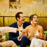 Relaxed engaged couple laughing together with friends during a luxury outdoor wedding celebration, capturing the joy and connection behind stress-free wedding planning.