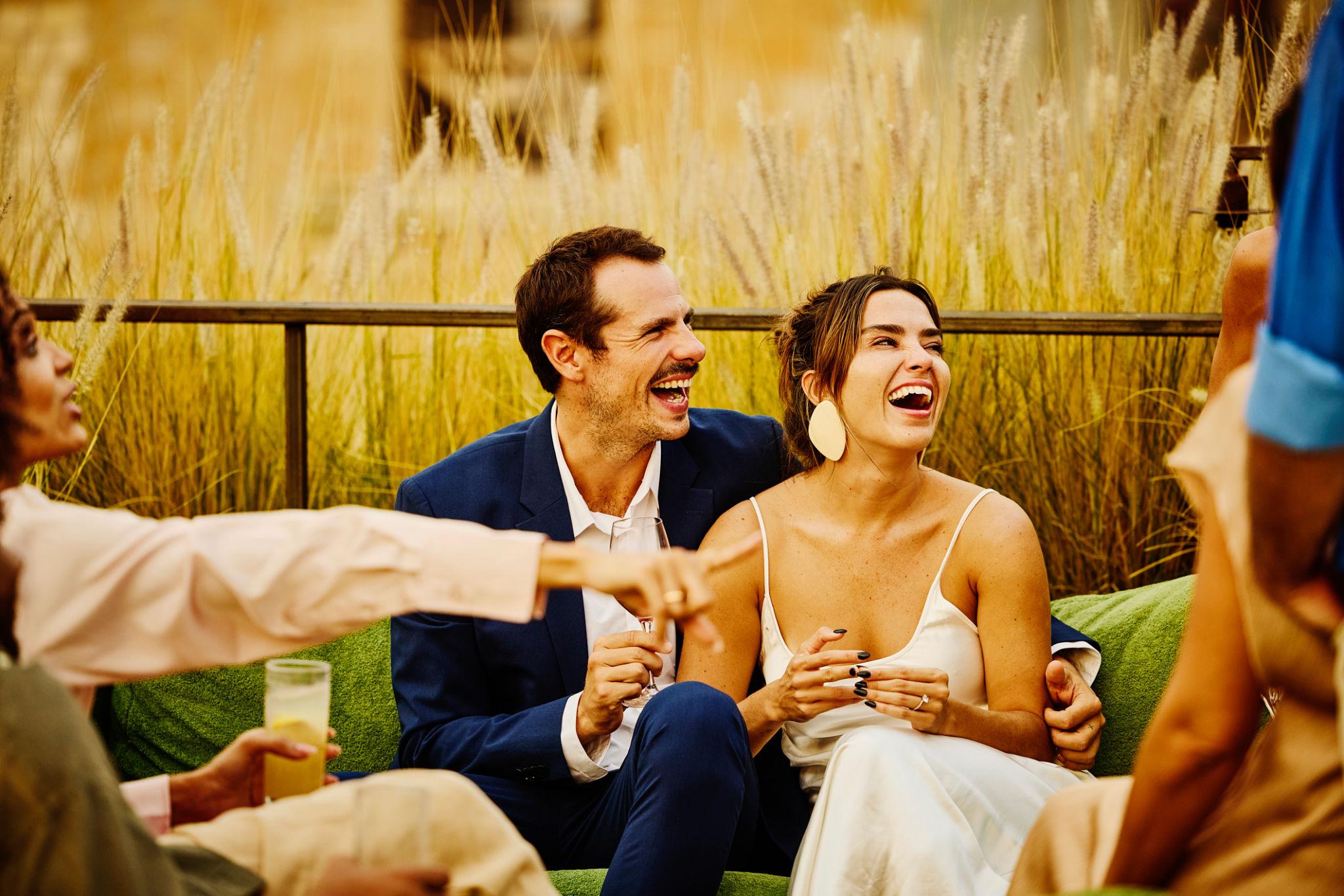 Relaxed engaged couple laughing together with friends during a luxury outdoor wedding celebration, capturing the joy and connection behind stress-free wedding planning.
