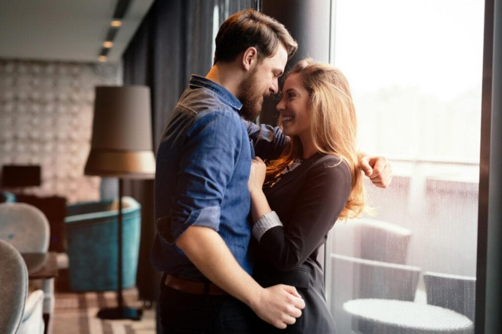 Newly engaged couple sharing a romantic moment together by a window while celebrating the beginning of their wedding planning journey.