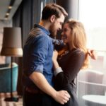 Newly engaged couple sharing a romantic moment together by a window while celebrating the beginning of their wedding planning journey.