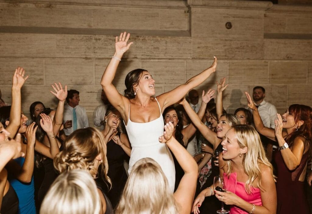 Bride celebrating on a packed dance floor surrounded by excited wedding guests during an energetic luxury wedding reception