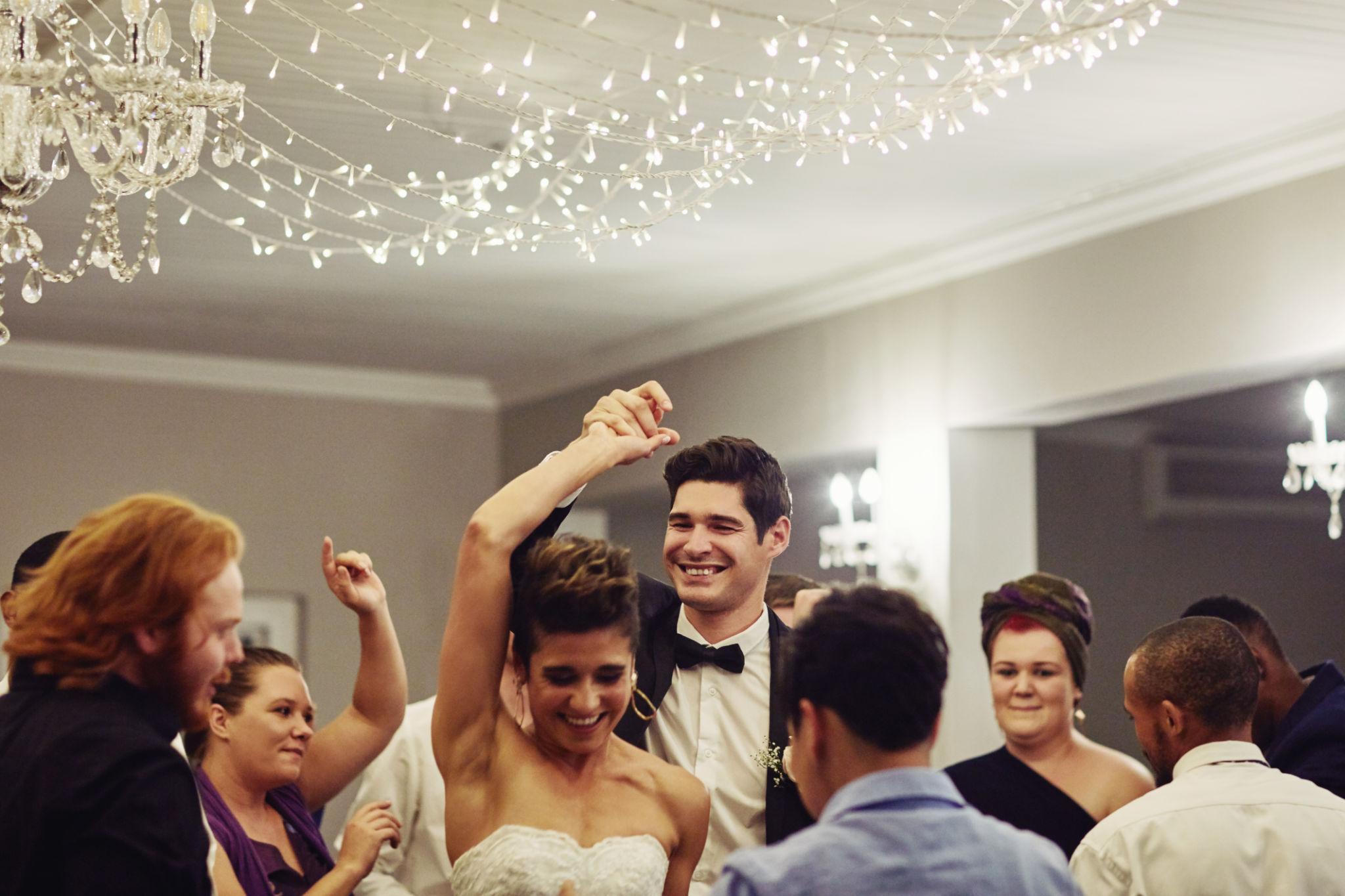 Bride and groom celebrating with guests on a packed dance floor during an elegant wedding reception