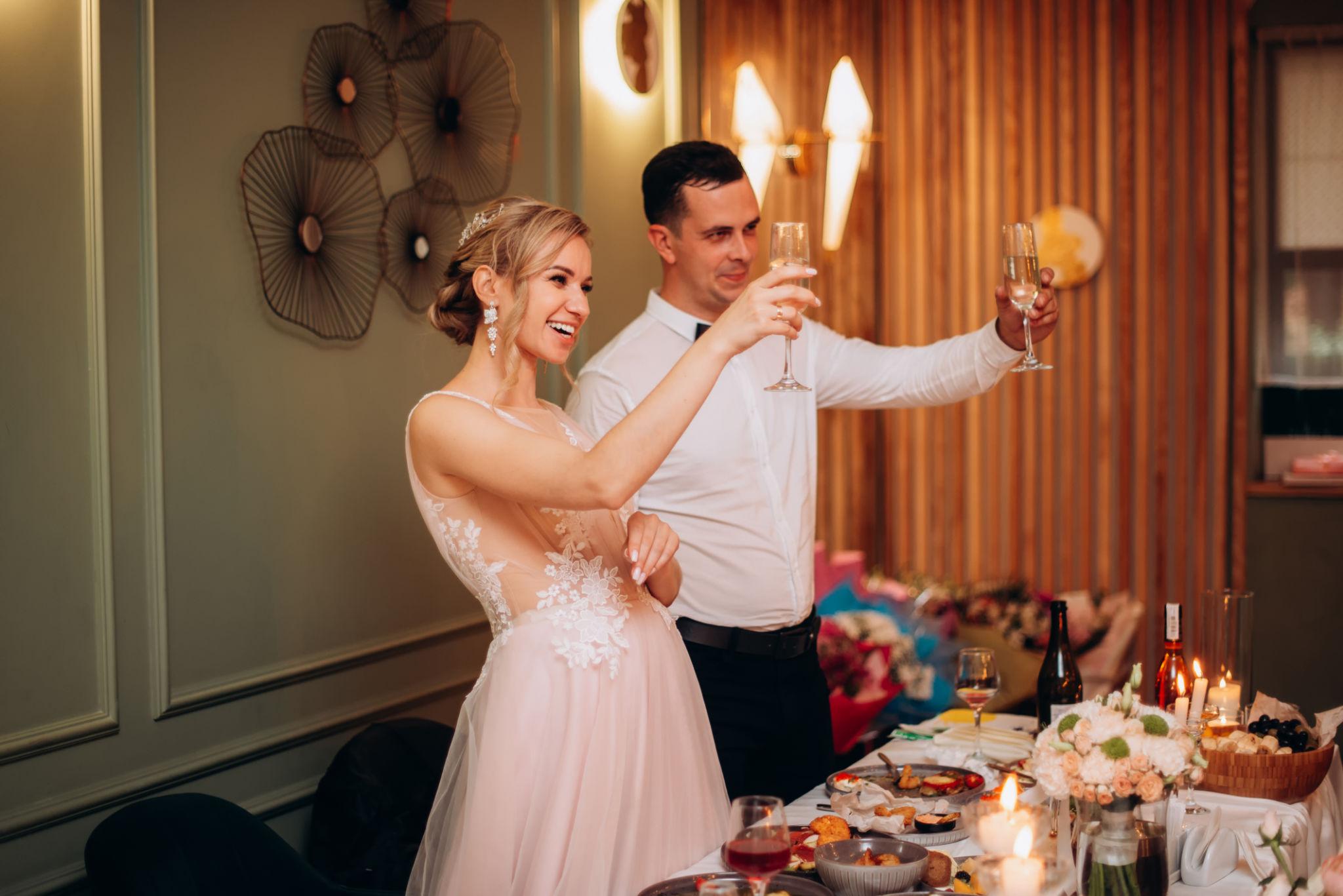 Newlywed couple smiling and raising champagne glasses during an elegant wedding reception celebration