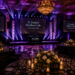 Elegant corporate gala ballroom setup featuring dramatic lighting effects, luxury table décor, illuminated stage columns, and premium event production.