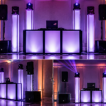 Clean professional wedding DJ setup featuring vertical illuminated columns, moving head lighting, ASUS ROG laptop, and EV ETX speakers in an elegant ballroom.